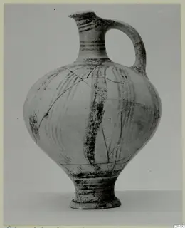 Round-bodied pottery vessel with a narrow neck and strap handle, painted with dark bands, photographed against a grey backdrop