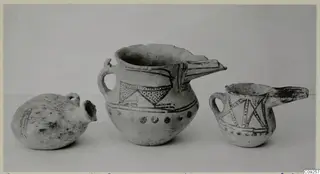Three painted pottery vessels with spouts and handles, shown side by side against a plain grey background.