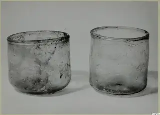 Two blown glass beakers with weathered, clouded surfaces standing side by side on a pale background.