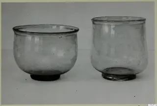 Two glass vessels side by side, one wide and rounded on the left, one taller on the right.