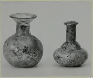 Two small blown glass vessels, one with a wide flared mouth and one with a long narrow neck, on a grey background.