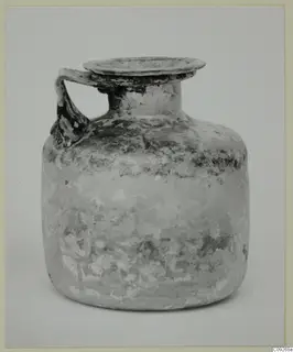 Blown glass jug with a single handle and a flared rim, photographed against a plain grey background