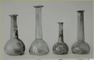 Four small blown glass bottles with long necks standing in a row against a grey backdrop.