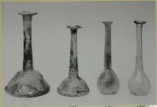 Four blown glass bottles with long necks and flared rims, shown side by side against a plain background.