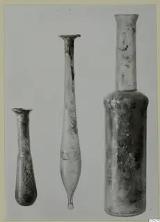 Three blown glass bottles, flasks and unguentaria standing in a row against a plain background