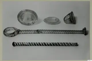 Five small objects on a light surface: an oval glass dish, a shallow dish, a cup fragment and two twisted rods, one with a ring at one end.