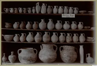 Pottery vessels from Politiko Tomb 1914 arranged on tiered wooden shelves: handled jugs, bowls and large jars.