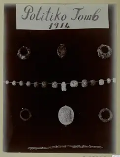Rings, beads and a carved oval stone from Politiko Tomb 1914, laid out on a dark background.