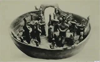 Terracotta bowl with an arched element at the back and many small standing figurines around its rim and inside.
