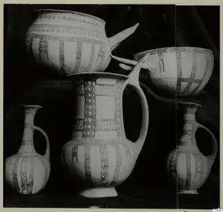 Group of painted pottery vessels: two bowls, a tall jug with handle, and two small jugs with handles, on a dark cloth.