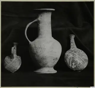 Three painted pottery vessels, a small flask, a tall jug and a bottle, standing on a dark draped cloth.