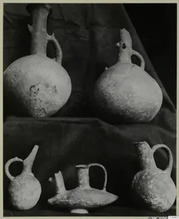 Five pottery jugs and juglets with handles and spouts, grouped on a dark cloth.