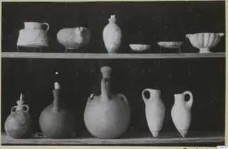 Pots and bowls displayed on two wooden shelves against a dark background