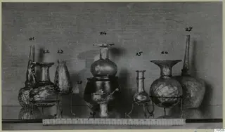 Several blown glass vessels on wire stands, with handwritten number labels and a scale ruler along the front