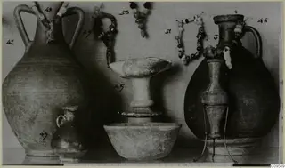 Group of vessels: two two-handled jugs, a small juglet, a stemmed dish and a bowl, with bead strands hanging behind.