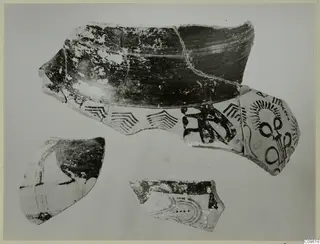 Three Levanto-Helladic pottery sherds with dark painted chevron bands and radiating motifs on a pale surface
