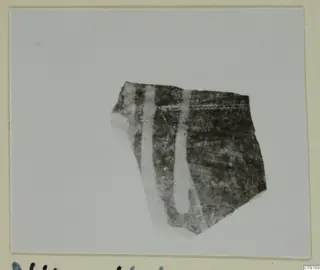 Pottery sherd from Nitovikla with two pale vertical bands on a dark surface, shown on a card mount.