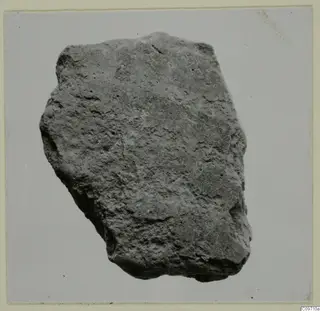 Pottery sherd, a rough irregular fragment with a pitted surface, photographed against a pale backdrop.