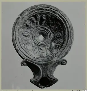 Terracotta oil lamp seen from above, with relief leaf and ring decoration around the filling hole and a nozzle with volute lugs at the base
