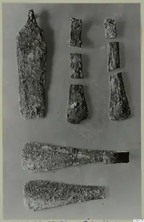 Several bronze tools and tool fragments laid out on a grey background