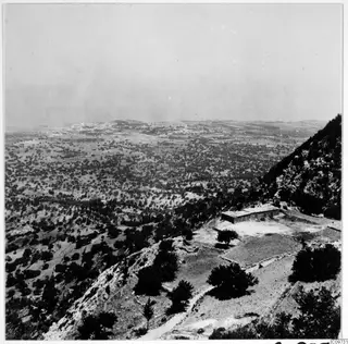 Mountain landscape in the Kyrenia Mountains, with a stone building and trees on a hillside above a wide plain