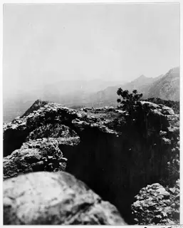 Rocky mountain landscape with a small shrub on an outcrop and hazy ranges beyond.