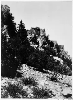 Ruined stone walls on a rocky hillside above bushes and pine trees in the Kyrenia Mountains.