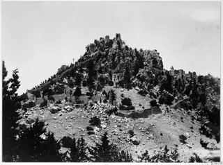 Ruined walls and towers on a rocky hilltop with pine trees in the Kyrenia Mountains