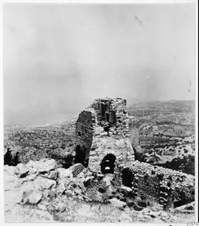 Ruined stone tower on a hilltop, with the sea and scrubby hills spread out below it