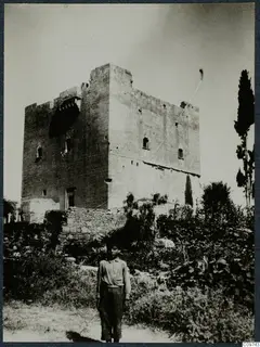 Tall square stone tower with a crenellated top, with a boy standing in the foreground