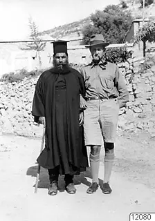 Papa Polivios and Einar Gjerstad standing side by side on a track in Mandres, with a stone wall behind them.