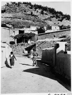 Village street at Lindros with mud-brick and stone houses, a woman walking and a man in shorts standing in the lane