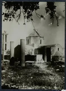 Domed building with a bell tower, two column drums in grass and a tree branch overhead, at Paphos