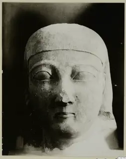 Limestone Cypro-Egyptian sculpture head and upper bust with a broken nose, seen against a dark background
