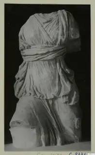 Headless draped statue torso in pale stone, photographed against a black background