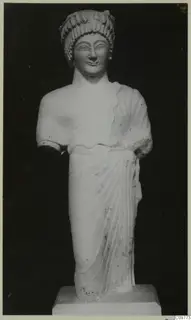 Limestone statue of a standing female figure with both arms broken off, on a square base