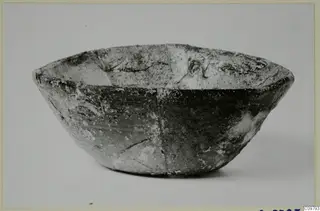 Deep rounded bowl with a flared rim, cracked and pale-encrusted, shown side-on against a plain background