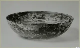 Cast glass bowl, shallow with rounded sides and pale weathered patches on a dark surface
