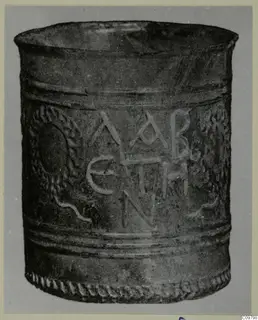 Blown glass beaker with raised letters in the centre and a wreath-like pattern on each side