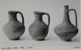 Three handled jugs of differing shapes standing in a row, photographed against a pale background.