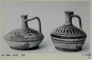 Two painted pottery jugs with single handles, side by side against a grey backdrop