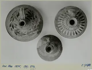 Three pottery vessels with handles and central openings, seen from above; two have dark painted patterns.