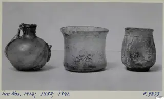 Three vessels of different shapes standing in a row on a pale surface against a grey backdrop