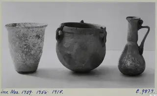 Three weathered vessels side by side: a flared beaker, a round two-handled pot and a small jug with a looped handle.