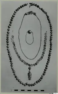 Three necklaces and pieces of jewellery laid out in loops on a grey backdrop, with a scale bar below.