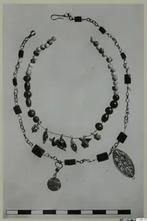 Necklaces and pendants of beads, chain and gold-coloured metal, laid out on a plain background.