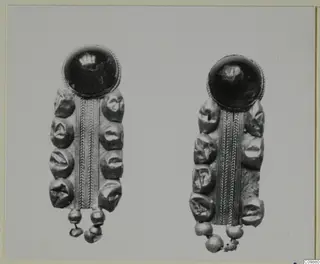 Two matching pieces of jewellery, each with a dark domed stone or glass top and a beaded metal plate, shown side by side