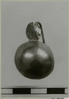 Small rounded piece of jewellery with a looped tube and a leaf-shaped plate on top, on a grey background.
