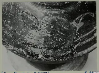 Close view of the rounded lower body and base of a dark-surfaced painted vessel, with worn decoration