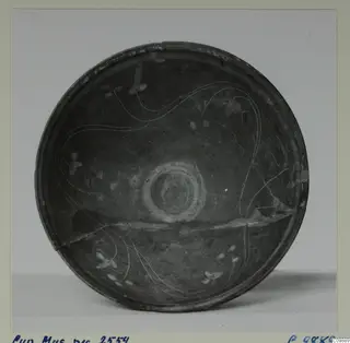 Shallow dark bowl seen from above, with thin pale curved lines and a ring of concentric circles at its centre.